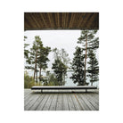 Een minimalistisch houten bankje staat op een ruim terras met uitzicht op pijnbomen en rustig water, omlijst door een modern dak - een uitnodigende scène rechtstreeks uit het Cozy Publishing Happy Homes Hideaways Boek.