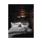 Een knus bed met wit en grijs beddengoed staat tegen rustieke houten muren en weerspiegelt de charme van Finse zomerhuizen. Op een plank daarboven ligt het Cozy Publishing Happy Homes Hideaways Boek, dat bijdraagt aan de uitnodigende sfeer onder een zacht gloeiende lamp.