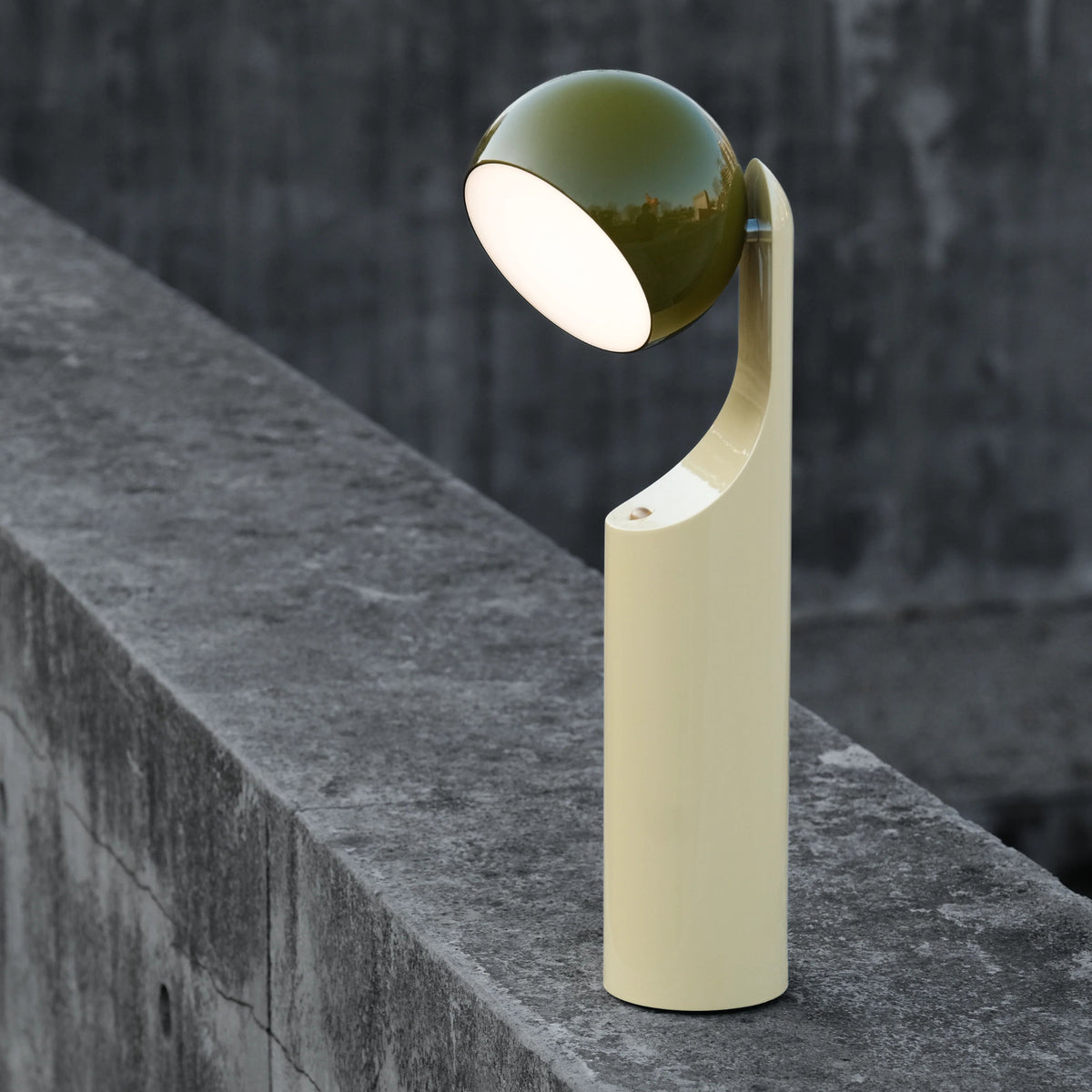 De Fine Lumens Mono Leeslamp LED Oplaadbaar in olijfgroen-geel van Fine Lumens heeft een modern minimalistisch ontwerp. De dimbare LED werpt een zacht wit licht terwijl hij op beton staat met zijn unieke koepelkap en crèmekleurige voet.