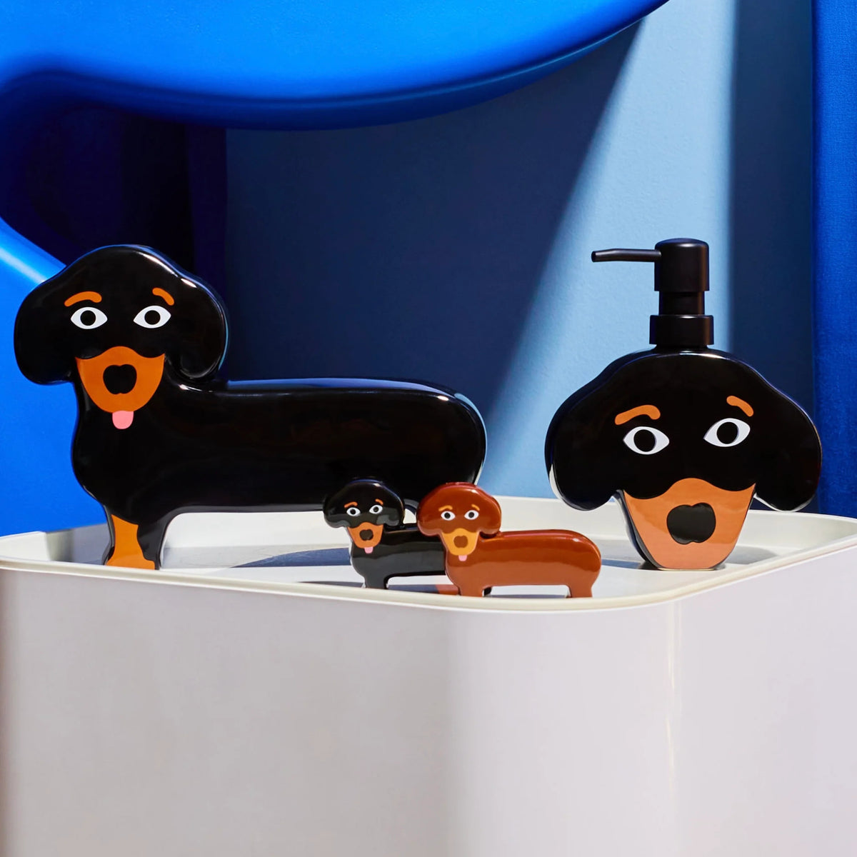 Kleurrijke Fluid Market Zout- en Pepervaatjes Teckel 2 st. en bijpassende bakjes in cartoonstijl staan op een wit oppervlak met een blauwe abstracte achtergrond - perfect als uniek designcadeau.
