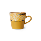 De HK Living 70s Ceramics Americano Mok Sunbeam is een retro-mok met een gele onderkant en een gespikkelde crèmekleurige en bruine bovenkant, en een afgeronde oor – ideaal voor je Americano. Afgebeeld op een effen witte achtergrond.