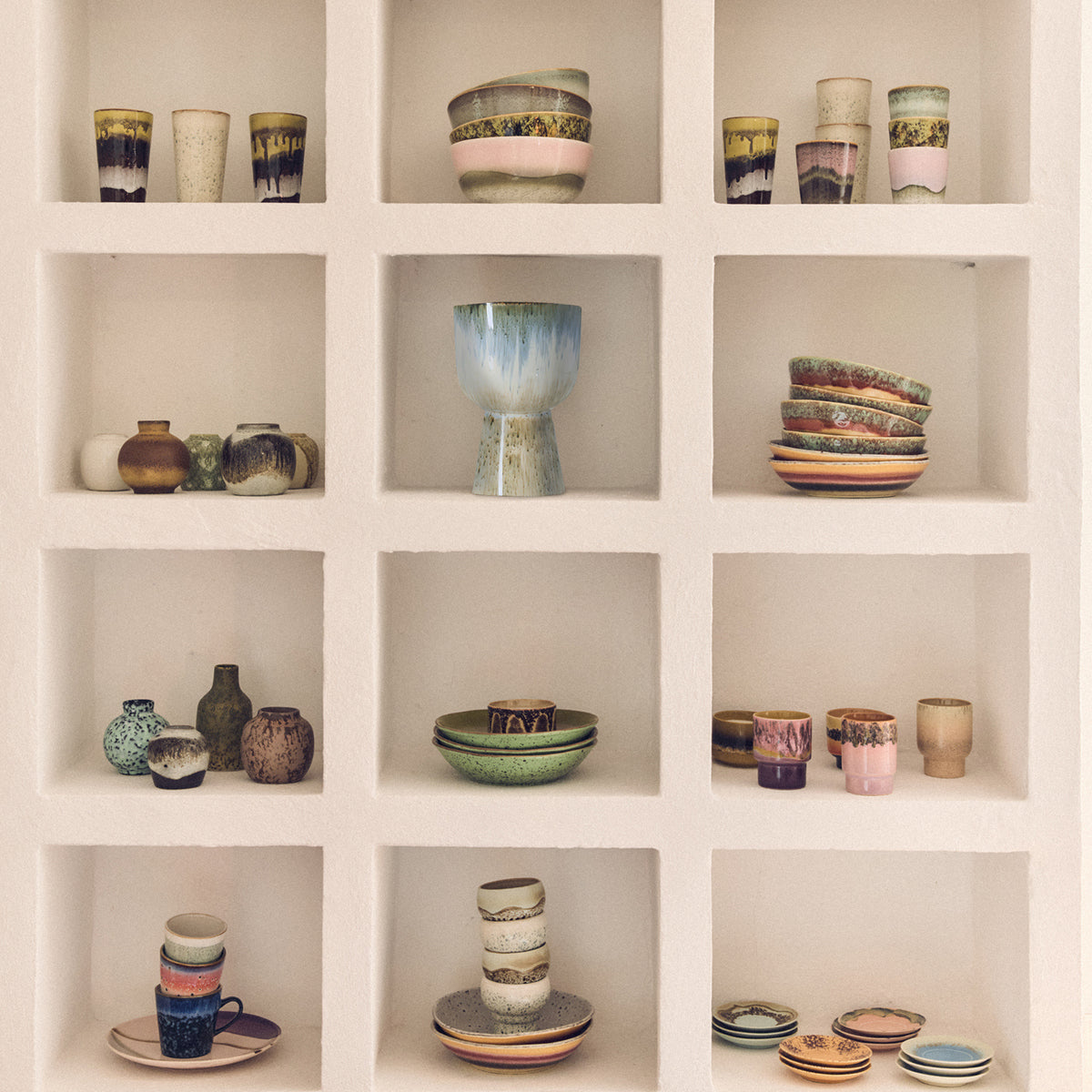 Een witte ingebouwde plank met twaalf vierkante vakjes toont kleurrijke HK Living 70s Ceramics Koffiekop Bramble - elk met de hand gemaakt met unieke texturen, netjes gerangschikt in elk vakje.