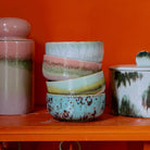 Een stapel van vier HK Living 70s Ceramics Dessertkom Impression kommen staat op een oranje plank naast twee potten met deksels, elk met unieke pastelpatronen uit de kleurrijke HK Living collectie.