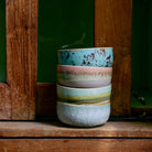 De HK Living 70s Ceramics Dessertkom Impression set van 4 kommen, elk met unieke pastelpatronen, is gestapeld op een rustieke houten vensterbank tegen weelderig groen.