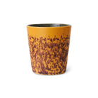 De HK Living 70s Ceramics Koffiekop Bay heeft een geel en bruin gemarmerd ontwerp, een gladde taps toelopende vorm en een glanzende afwerking, die retro stijl weerspiegelt. Afgebeeld tegen een effen witte achtergrond.