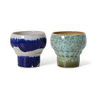 De HK Living 70s Ceramics Lungo Mokken Symbolist set bestaat uit twee moderne, ambachtelijke mokken van keramiek: de ene glanzend blauw met wit, de andere gespikkeld lichtgroen met bruin, beide met brede randen in ware HK Living stijl.