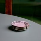Een stapel van vier HK Living 70s Ceramics Schotel Koffiekop Doodle D11 ligt op een ronde, lichtgroene tafel tegen een vage achtergrond.