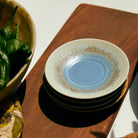 Een stapel van drie HK Living 70s Ceramics borden met blauw en bruin glazuur rust op een houten oppervlak; ernaast staat een deel van een schaal met groene paprika's. Combineer met HK Living 70s Ceramics Schotel Koffiekop Ocean D11 voor een perfecte tafelsetting.