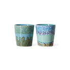 De HK Living 70s Ceramics Van Gogh Koffiekop Self Portrait set (2 stuks) heeft artistieke blauwe en groene glazuren met golvende, gestructureerde ontwerpen bij de randen en bodems, naast elkaar weergegeven op een witte achtergrond.