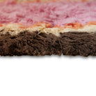 Close-up van de HK Living Fluffy Tapijt Downtown 180/120, met het gestructureerde, ruige oppervlak en de horizontale strepen in bruin, beige, oranje en roze tinten tegen een witte achtergrond.