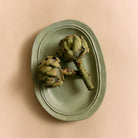 Twee verse artisjokken rusten op een HK Living New Classics Schaal Muntgroen L, onderdeel van de keramische serviescollectie van HK Living, tegen een beige achtergrond.