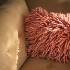 Het HK Living Rugged Kussen Roze 70/45 kussen voegt een vleugje roze toe aan een bruine corduroy fauteuil, terwijl zacht zonlicht zachte schaduwen creëert op het oppervlak van de stoel.