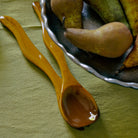 De HK Living Saladebestek Oker 2 st., een glanzend bruine bestekset, rust op een groen tafelkleed naast een donkere kom met golvende randen - een ideaal cadeau van HK Living.