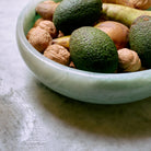 Een HK Living Saladekom Mint D26 van HK Living, gevuld met avocado's, walnoten en peren, staat op een grijs gestructureerd oppervlak.