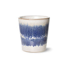 De HK Living 70s Ceramics Koffiekop Cosmos is een keramische beker met een licht taps toelopende vorm, glanzend witte basis en blauw penseelstreek-achtig structuurglazuur rond het midden, geïnspireerd op retro design. Afgebeeld tegen een effen witte achtergrond.