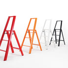 Vier moderne Hasegawa Lucano 3 Step ladders in rood, oranje, wit en zwart staan op een rij tegen een witte achtergrond. Het gedurfde zwarte ontwerp van Hasegawa voegt een opvallend contrast toe aan de minimalistische Japanse stijl van deze collectie.