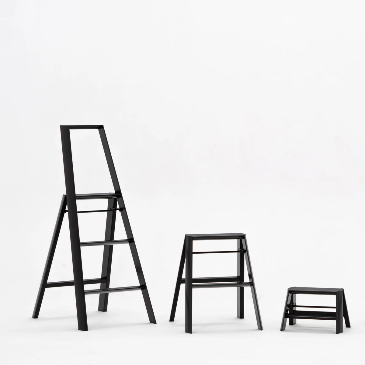 Drie Hasegawa zwart trapkrukken-Lucano Ladder 3 Trede, een hogere viertrede en een kleine tweetrede- worden weergegeven op een witte achtergrond, waardoor hun slanke zwarte ontwerp wordt benadrukt.
