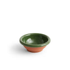 De Hay Barro Kom Groen D21 van Hay heeft een klein, rond terracotta ontwerp met een glanzende donkergroene binnenkant en rand, gecontrasteerd door een matte terracotta buitenkant, die doet denken aan Portugees servies, op een effen witte achtergrond.