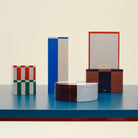 De Hay Blikken Doos Blauw Off-White Slim van Hay staat op een blauw oppervlak tegen een neutrale achtergrond en toont modern Scandinavisch design met gedurfde blauwe en gebroken witte kleuraccenten.