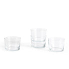 Vier Hay Glas Helder S-kopjes zijn gerangschikt op een wit oppervlak. Met een minimalistisch ontwerp is één paar ruimtebesparend gestapeld, terwijl de andere twee kleine glazen naast elkaar staan.
