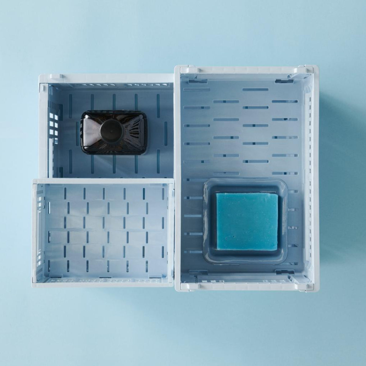Twee Hay Kleur Krat Mini Lichtblauw manden van Hay staan op een blauw oppervlak. De linker bevat een klein donker flesje, de rechter een doorzichtig bakje met een blauw zeepstaafje. Beide manden zijn gemaakt van gerecycled plastic.