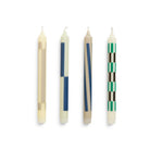 De Hay Patroon Kaarsen Crème en Donker 4 st. van Hay heeft vier rechtopstaande witte kaarsen, elk met unieke geometrische patronen in beige, blauw, bruin en groen - ideaal voor cadeauverpakkingen.