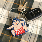Een set sleutels, met een autosleutel en de Hightide Stitch Work Sleutelhanger Sumo Worstelaar van Hightide, met een geborduurde sumoworstelaar in een rode mawashi, zit op geruite stof.