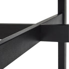 Close-up van kruisende zwarte balken van het Hubsch Fjord Eettafel Essenhout Zwart D120 frame, tegen een witte achtergrond.