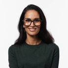 Een vrouw met lang donker haar, die een Izipizi Leesbril Office Zwart van Izipizi draagt en een donkergroene trui, glimlacht naar de camera tegen een effen witte achtergrond.