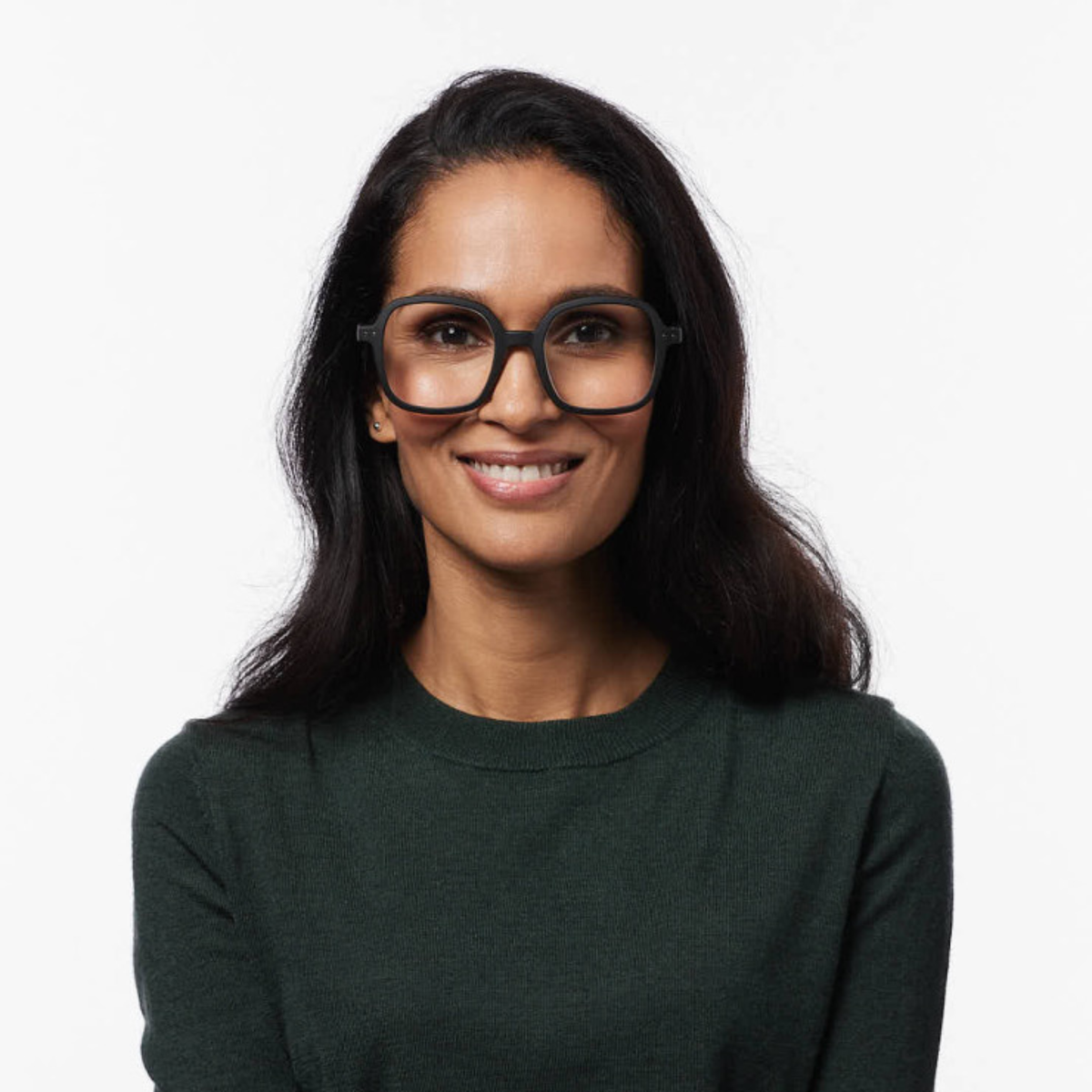 Een vrouw met lang donker haar, die een Izipizi Leesbril Office Zwart van Izipizi draagt en een donkergroene trui, glimlacht naar de camera tegen een effen witte achtergrond.
