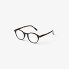 De Izipizi Leesbril #D Tortoise van Izipizi heeft een ronde bril met een donker tortoiseshell montuur en heldere glazen, afgebeeld op een effen witte achtergrond.
