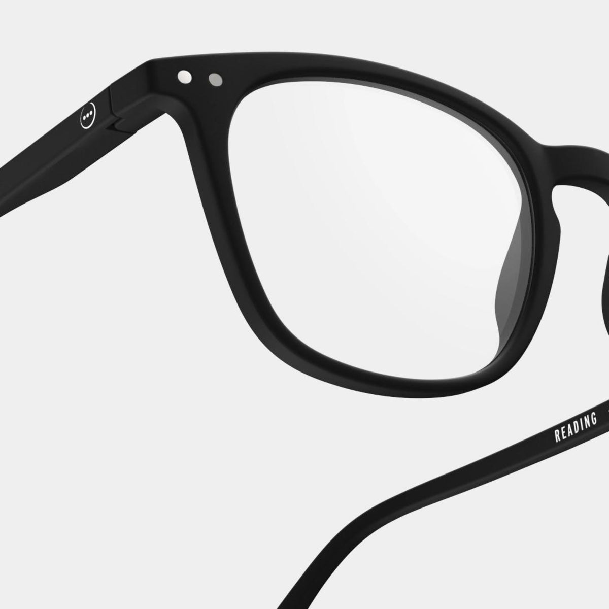 Close-up van Izipizi Leesbril #E Zwart montuur met heldere glazen, met linksboven en op de veerarm witte tekst READING en een rond logo - waardoor deze Izipizi leesbril een stijlvolle keuze is voor elke look.