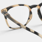 Close-up van de Izipizi Leesbril #E Light Tortoise van Izipizi, een stijlvolle leesbril in schildpad beige, bruine en zwarte tinten voor mannen en vrouwen, afgebeeld tegen een effen lichte achtergrond.