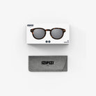 Een doosje met de Izipizi Zonnebril Sterkte #C Tortoise en Izipizi branding zit boven een grijze softcase met IZIPIZI erop gedrukt, beide op een witte achtergrond. Deze unisex zonnebril biedt UV-bescherming.