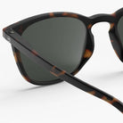 Close-up van de Izipizi Zonnebril #E Tortoise van Izipizi, met donkere glazen en een mat zwart schildpadmontuur met UV-bescherming, tegen een effen witte achtergrond.