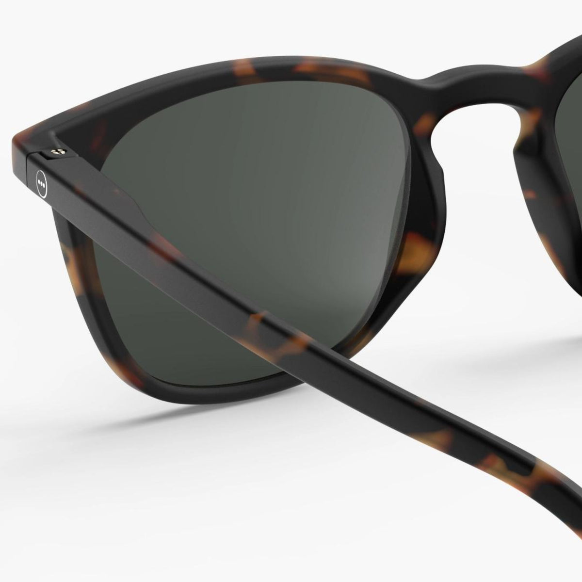Close-up van de Izipizi Zonnebril #E Tortoise van Izipizi, met donkere glazen en een mat zwart schildpadmontuur met UV-bescherming, tegen een effen witte achtergrond.