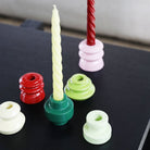 Kleurrijke ronde kandelaars van keramiek tonen twee spiraalvormige &Klevering Bravo Kaarsen Rood 3 st., één geel en één rood. Ideaal als uniek cadeau of om de handgeschilderde kaarsen van &Klevering in te zetten.