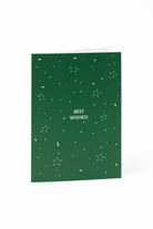 De Matriks Kerst- en Nieuwjaarskaart Best Wishes! heeft een groen ontwerp van Julie Lindekens, met rode, gele en witte confetti-achtige vormen en vetgedrukte witte "BEST WISHES!" tekst in het midden. Merk: Matriks.