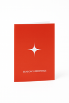 De Matriks Kerst- en Nieuwjaarskaart Season's Greetings van Matriks staat rechtop in rood, met een witte ster boven de vetgedrukte tekst "SEASON'S GREETINGS" en een strakke witte achtergrond voor een feestelijke, minimalistische look.