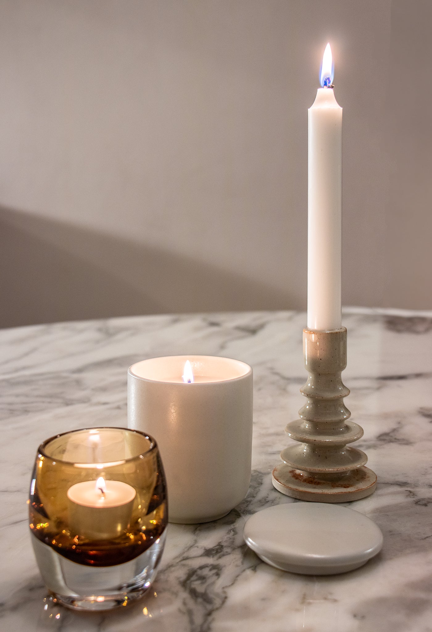 Een Matriks Fragrances Geurkaars Keramiek Sweet & Smokey 270 g, handgemaakt in Antwerpen, is aangestoken op een wit marmeren oppervlak in een keramieken potje.