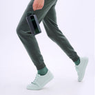 Persoon in groengrijze joggingbroek en mintgroene gympen loopt met een Nalgene Drinkfles Brede Opening Jade 1L waterfles aan zijn zijde. Alleen het onderlichaam en de hand zijn te zien tegen een lichte achtergrond. Merk: Nalgene.