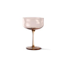 De Paveau Swirl Champagne Coupe Glow Beige 26 cl van Paveau heeft een doorschijnende, lichtbruine brede schaal en slanke steel, die een subtiele gloed uitstraalt tegen een effen witte achtergrond.