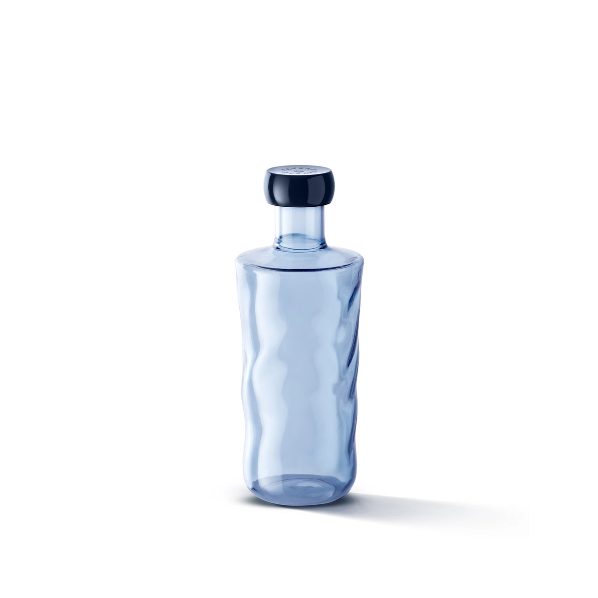 Een Paveau Swirl Waterfles Midnight Blauw 0,75 l van Paveau rust op een wit oppervlak. Het helderblauwe borosilicaatglas heeft subtiele golven en een ronde stop, die een zachte schaduw werpen die een elegante middernachtelijke toets toevoegt.