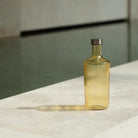 De Paveau Waterfles Cable Yellow 1,25 l van Paveau, met een geribbeld amberkleurig design en metalen kap, rust op een licht stenen oppervlak met een lange schaduw; water en neutrale muren vervagen op de achtergrond.