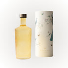Een hoge, heldere geribbelde Paveau Waterfles Cable Yellow 1,25 l met gouden vloeistof en een metalen dop staat naast een cilindrische witte Paveau houder versierd met pauwen, bloemen en vlinders.