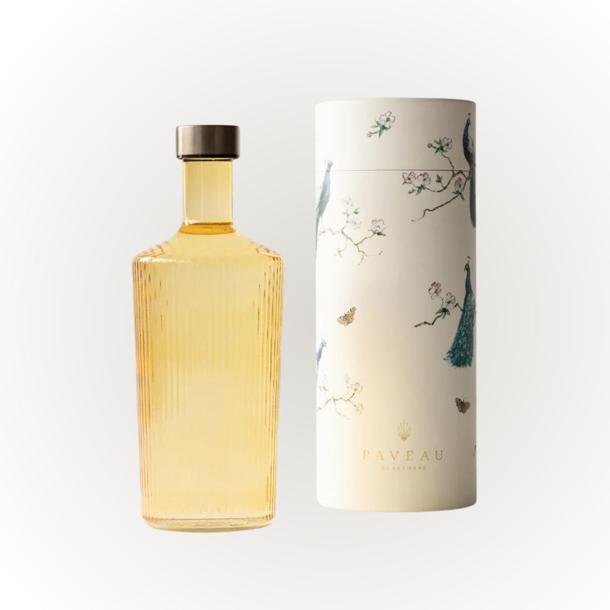 Een hoge, heldere geribbelde Paveau Waterfles Cable Yellow 1,25 l met gouden vloeistof en een metalen dop staat naast een cilindrische witte Paveau houder versierd met pauwen, bloemen en vlinders.