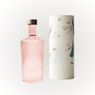 De Paveau Waterfles Pink 1,25 l met geribbeld design en metalen dop staat naast zijn witte cilindrische doos, versierd met illustraties van pauwen, takken en vlinders en de merknaam Paveau.