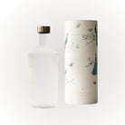 Een heldere, elegante Paveau Waterfles White Haven 1,25 l met een metalen dop staat naast een cilindrische doos versierd met pauwen en vlinders. Beide, met het merk Paveau, staan tegen een effen witte achtergrond.