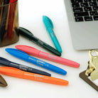 Een Penco Glider Pen Blauw rust op een wit bureau in de buurt van een zilveren laptop, een bruin klembord met gouden clip en een bruine penhouder. Geniet van een zijdezachte schrijfervaring bij elke streek met deze Penco pen.