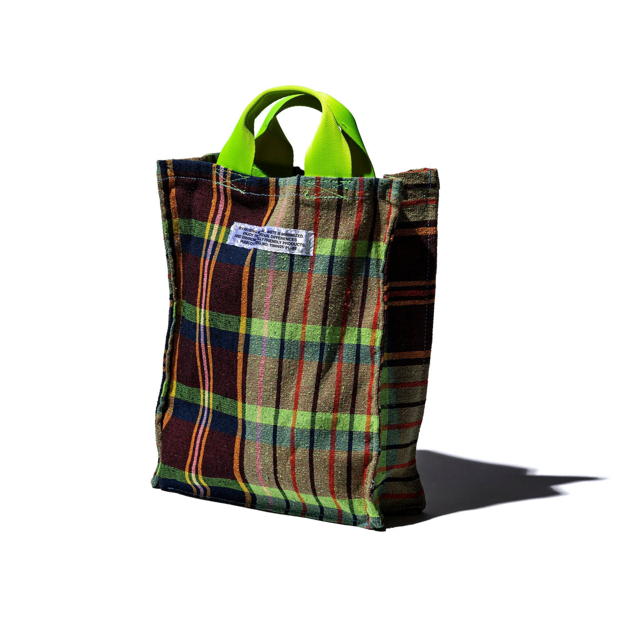 De Puebco Check Document Tas van Puebco is een kleine documententas gemaakt van gerecycleerde stoffen, met groene handgrepen en een kleurrijk ruitpatroon in groen, rood en geel, rechtopstaand op een witte achtergrond met schaduw naar rechts.